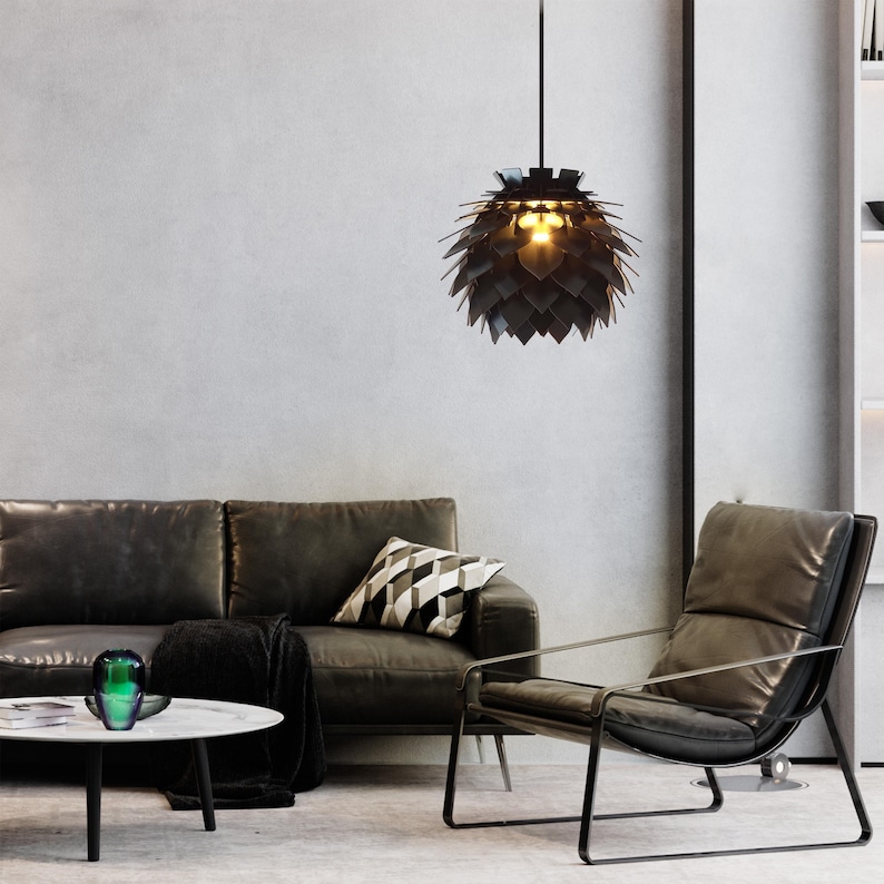 May include: A modern living room with a black leather sofa, a matching armchair, and a round white coffee table. A decorative black pendant light hangs from the ceiling. A throw pillow with a geometric pattern rests on the sofa.