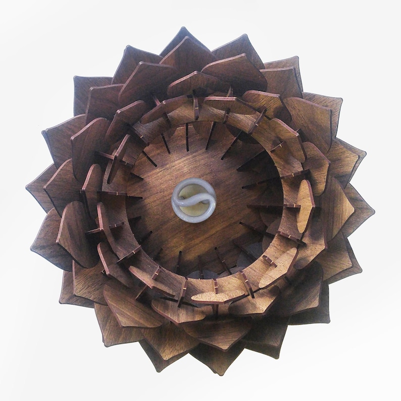 May include: A wooden, flower-shaped light fixture with a warm brown finish. The fixture features layered, petal-like elements surrounding a central light bulb. The design is intricate and geometric, creating a unique decorative piece.