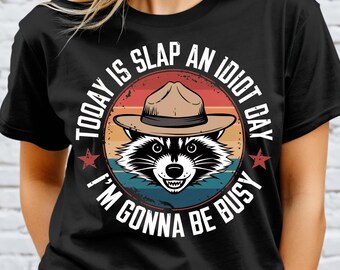 May include: Black t-shirt featuring a vintage-style graphic of a raccoon wearing a ranger hat. The graphic reads "Today is slap an idiot day I'm gonna be busy".