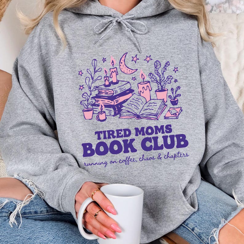 May include: A gray hoodie with a purple and pink graphic that reads "Tired Moms Book Club" with illustrations of books, candles, and plants. The text "running on coffee, chaos & chapters" is below the book club text.