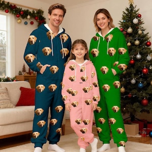 Può includere: Tre persone che indossano pigiami a tuta con cappuccio abbinati. I pigiami sono verde acqua, rosa e verde, ciascuno ricoperto da immagini di un Golden Retriever. La famiglia è in piedi davanti a un albero di Natale.