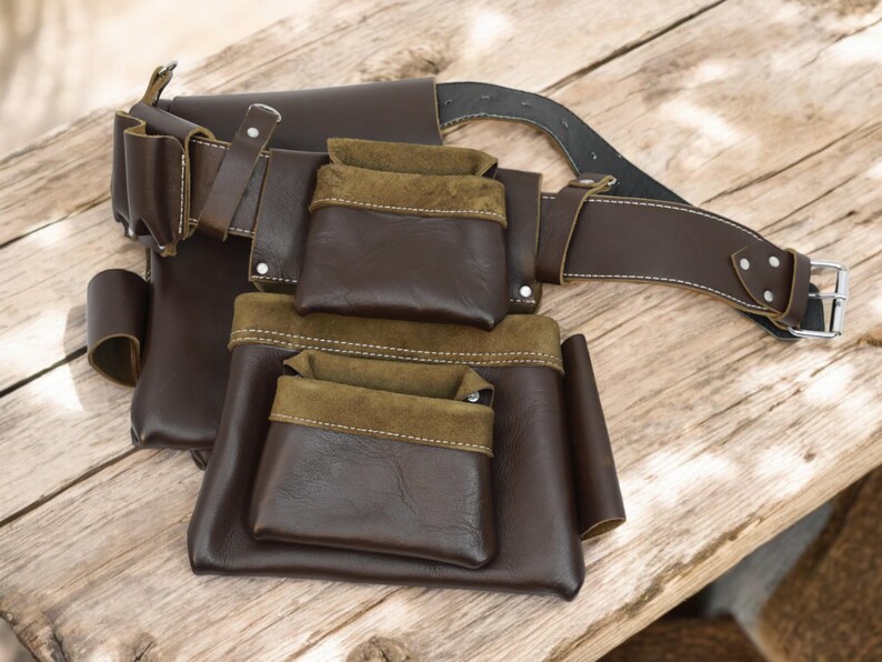 May include: A brown leather tool belt with multiple pockets and a brown leather belt with a silver buckle.