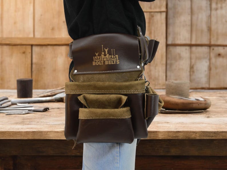 May include: A brown leather tool belt with multiple pockets and a brown suede flap. The belt has a gold logo that reads "Bolt Belts" with a graphic of tools above the text.
