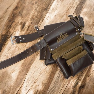 May include: A brown leather tool belt with multiple pockets and a brown leather belt with a silver buckle. The belt has the text "Legler Tool Belts" embossed on it.