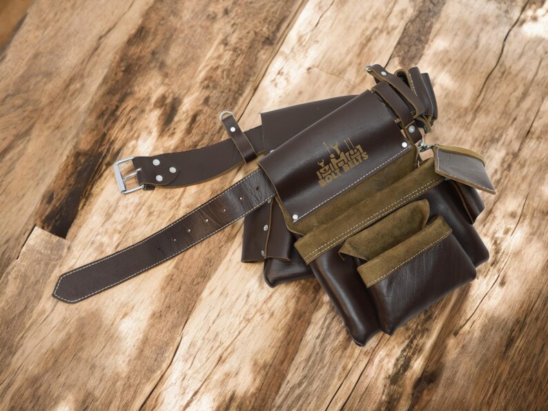 May include: A brown leather tool belt with multiple pockets and a brown leather belt with a silver buckle. The belt has the text "Legler Tool Belts" embossed on it.
