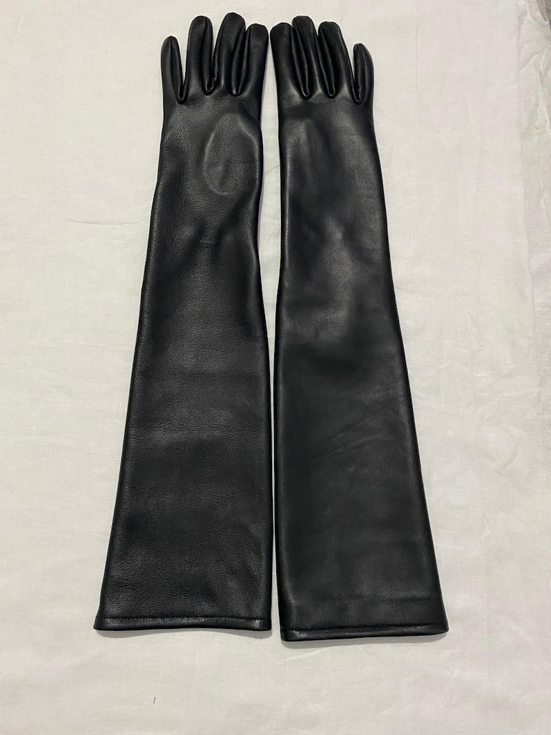 May include: A pair of long, black leather gloves. The gloves are sleek and reach well past the elbows. The leather appears smooth and the gloves are laid out on a white surface.