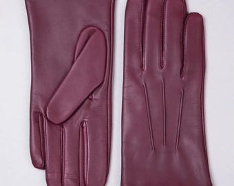 Peut inclure: Une paire de gants en cuir bordeaux. Les gants sont présentés sur un fond blanc. Les gants ont un design classique avec une texture lisse et des détails de couture visibles. Les gants sont d'une nuance de bordeaux profonde et riche.