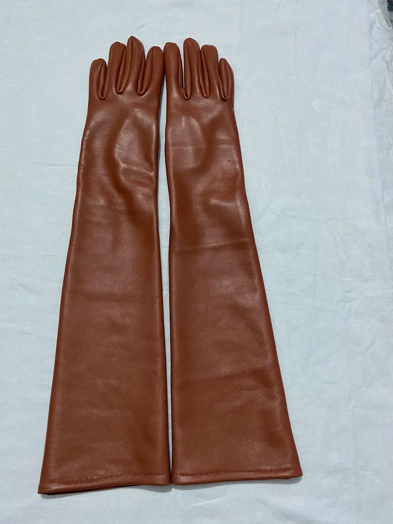 May include: A pair of long, brown leather gloves. The gloves are a warm, reddish-brown color and extend well past the wrist. The fingers are individually shaped, and the leather appears smooth and supple.
