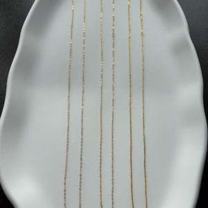 May include: Three delicate gold-toned necklaces with fine link chains, each featuring a small circular clasp at the top. The necklaces are arranged vertically, displaying a consistent metallic finish and a simple, slender design structure.