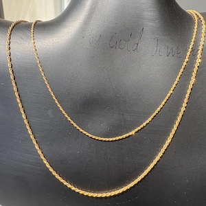 Könnte beinhalten: Eine goldene Kordelkette mit gedrehtem, texturiertem Glieddesign. Die Kette wird auf einer schwarzen Schaufensterpuppe präsentiert und zeigt ihr metallisch gelbes Finish sowie das komplexe, spiralförmige Muster.