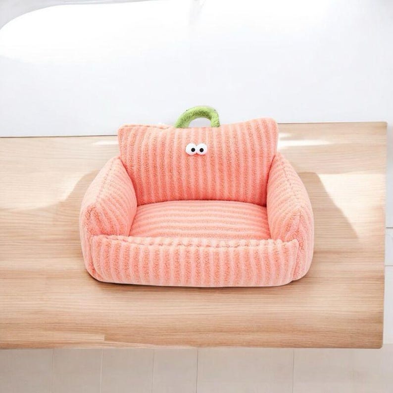 Peut inclure: Un lit pour animal de compagnie en peluche ray&eacute; rose et blanc en forme de canap&eacute; avec une poign&eacute;e en boucle verte et deux yeux blancs.