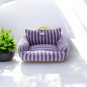 Peut inclure: Lit de compagnie en forme de canap&eacute; &agrave; rayures violettes et jaunes avec deux yeux globuleux.