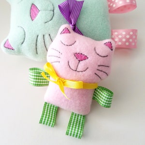 May include: Two plush cat toys, one light blue with purple ribbon and white polka dot ribbon, and one pink with yellow ribbon and green gingham ribbon.