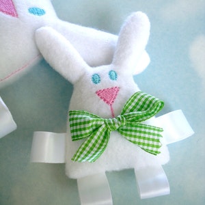 May include: White bunny plush toy with green and white gingham bow, blue and pink embroidered eyes, and white satin ribbon ties.