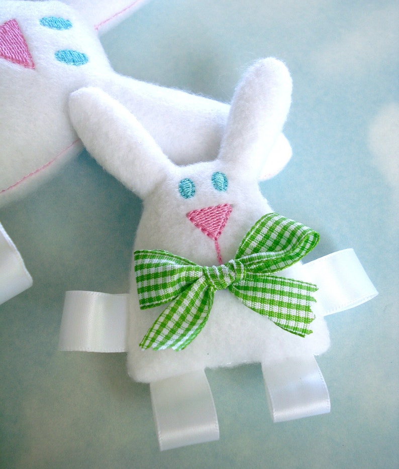 May include: White bunny plush toy with green and white gingham bow, blue and pink embroidered eyes, and white satin ribbon ties.