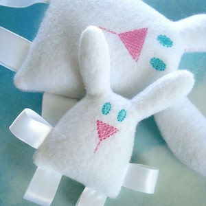 May include: Two white plush bunny toys with embroidered pink and blue details. The bunnies have white satin ribbons attached to their limbs.