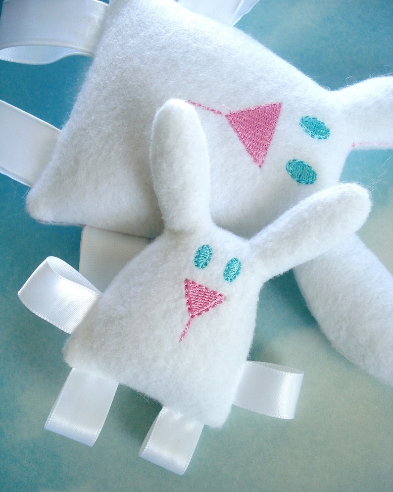 May include: Two white plush bunny toys with embroidered pink and blue details. The bunnies have white satin ribbons attached to their limbs.