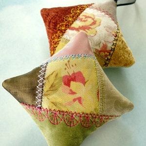 Può includere: Due ornamenti in patchwork fatti a mano, uno con retro in velluto verde e bordo smerlato, l'altro con retro in velluto marrone. Entrambi gli ornamenti presentano motivi floreali e sono decorati con ricami.