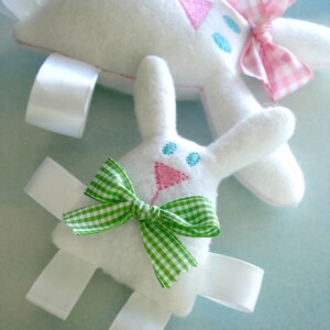 May include: Two white felt bunny toys with embroidered details. One bunny has a pink and white gingham bow and the other has a green and white gingham bow.