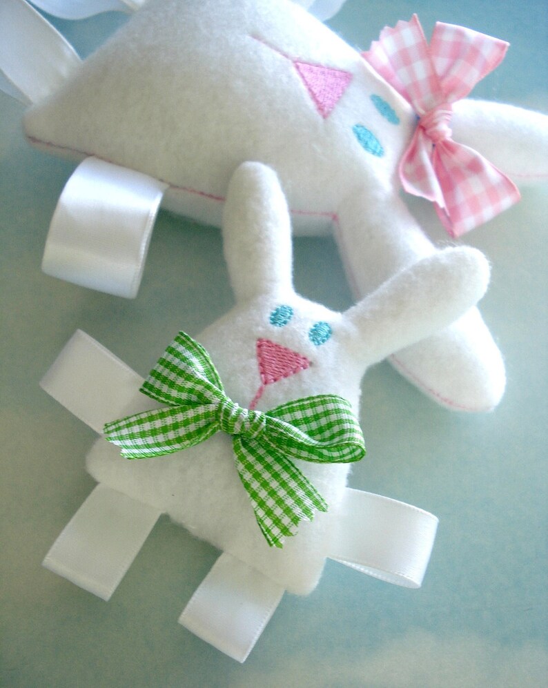 May include: Two white felt bunny toys with embroidered details. One bunny has a pink and white gingham bow and the other has a green and white gingham bow.