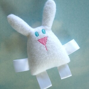 May include: White plush bunny toy with embroidered blue eyes and a pink nose. The bunny has white satin ribbon arms and legs.