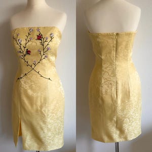Puede incluir: Un vestido amarillo sin tirantes con un dise&ntilde;o de bordado floral. El vestido tiene una silueta ajustada y una abertura en la parte delantera.
