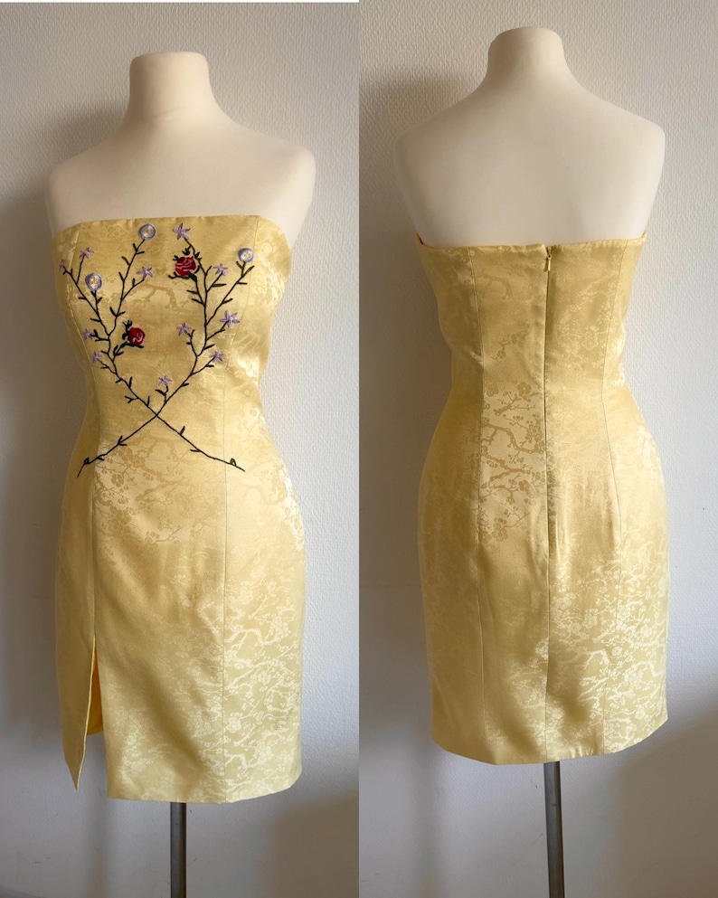 Puede incluir: Un vestido amarillo sin tirantes con un dise&ntilde;o de bordado floral. El vestido tiene una silueta ajustada y una abertura en la parte delantera.