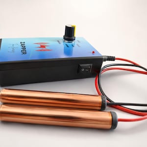 Pode incluir: Um dispositivo eletrónico preto com a etiqueta ZAPPER, um topo com gradiente azul, um botão de controlo rotativo e uma luz indicadora vermelha. Possui um interruptor preto na lateral e está ligado a dois punhos cilíndricos de cobre através de fios vermelhos e pretos.