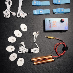 May include: A collection of electronic health devices, including a control box labeled "ZAPPER", blue straps, white earbud sets, electrode pads, and copper hand cylinders. The items are arranged on a black surface.
