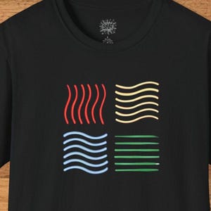 May include: Black t-shirt featuring a colorful graphic of the four elements: fire, air, water, and earth. The fire element is represented by red wavy lines, air by yellow wavy lines, water by blue wavy lines, and earth by green horizontal lines. The shirt has the brand name "SPLAT" printed on the collar.