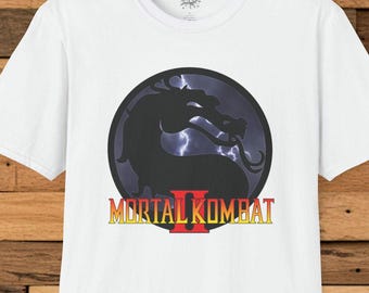 Könnte beinhalten: Weißes T-Shirt mit dem Mortal Kombat II-Logo. Das Design zeigt eine schwarze Drachensilhouette vor einem stürmischen Hintergrund, mit dem Spieltitel in Gelb und Rot.