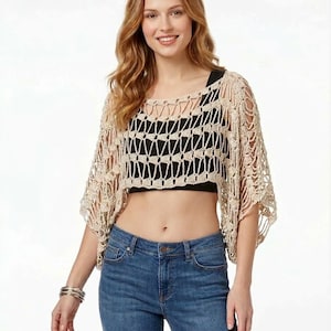 Könnte beinhalten: Beige Häkeltop mit quadratischem Ausschnitt und kurzen Ärmeln. Das Top wird über einem schwarzen Top getragen und mit einer blauen Jeans kombiniert. Das Häkeldesign weist ein offenes, geometrisches Muster auf.