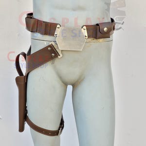 Op de afbeelding: Bruin leren riem- en holster set. De riem heeft een zilveren gesp en kleine zakjes. Een bijpassende holster is bevestigd aan een beenriem. De set is ontworpen voor cosplay of kostuumgebruik.