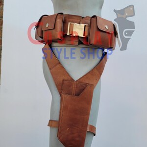 May include: Brown leather utility belt with multiple pouches and a gold-colored buckle. The belt includes a holster attached to suspenders. The text "STYLE SHOP" is visible on the belt.