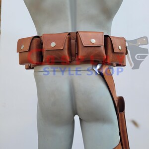 May include: A brown leather utility belt with multiple pouches and a leg strap. The belt features several square pouches with silver button closures. The leg strap has a small holster. The text "STYLE SHOP" is visible.