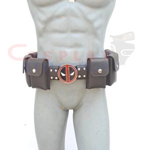 Könnte beinhalten: Ein brauner Ledergürtel mit einer silbernen Schnalle, die das Deadpool-Logo in Rot und Schwarz zeigt. Der Gürtel hat mehrere Taschen auf beiden Seiten.