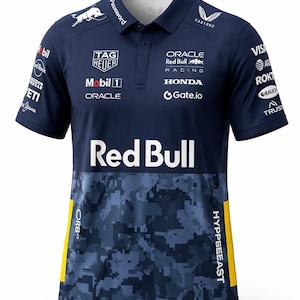 Puede incluir: Polo azul marino con el logo de Red Bull y patrocinadores. La parte inferior delantera presenta un patrón de camuflaje azul y detalles amarillos. Logos: Oracle, Honda y Visa. Cuello de camisa y mangas cortas.