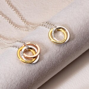 May include: Two necklaces featuring interlocking circular pendants in silver, gold, and rose gold tones. One pendant is engraved with "Mom Dad" and "Love you forever," while the other features the names "Jasmine" and "Zayne" with the date "28.07.2026."