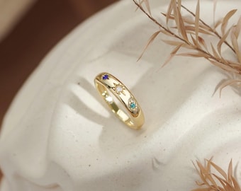Peut inclure: Une bague anneau en or ornée de trois petites gravures en forme d'étoile, chacune sertie d'une minuscule pierre précieuse de couleur bleue, transparente et turquoise. La bague présente une surface polie et brillante.