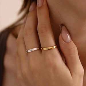 May include: Two rings, one gold and one silver, are displayed. The gold ring has the word "Hope" inscribed on it, while the silver ring has the word "Faith". The rings are simple bands, suitable for everyday wear.