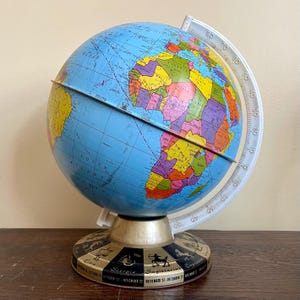 May include: A vintage globe with a blue ocean and colorful continents. The globe has a white meridian ring and a base featuring zodiac symbols. The globe is approximately 12 inches tall.