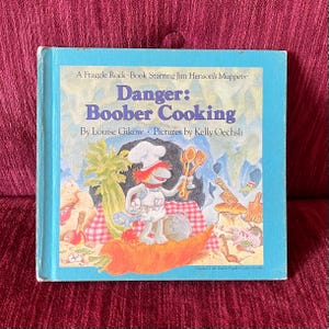 May include: A children's book titled "Danger: Boober Cooking" featuring a blue cover with a cartoon illustration of a Muppet character in a chef's hat. The book is part of the Fraggle Rock series.