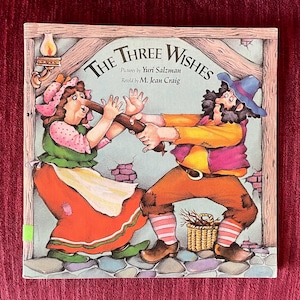 May include: A children's book cover titled "The Three Wishes" with illustrations of a man and woman struggling over a wooden object. The cover art is colorful, featuring a rustic background and whimsical character designs.