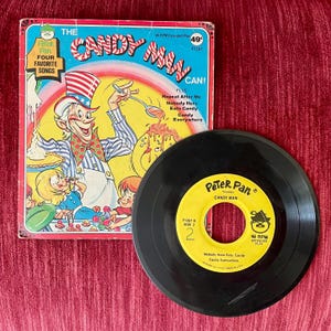 May include: A vintage Peter Pan Records 45 RPM record and sleeve. The sleeve features a colorful illustration of a candy man with children. The record is black with a yellow label that reads "Candy Man".