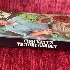 May include: A hardcover book titled Crockett's Victory Garden by James Underwood Crockett. The cover features a photograph of a person in a light blue shirt gardening. The spine and cover display the title in white text against a black background.