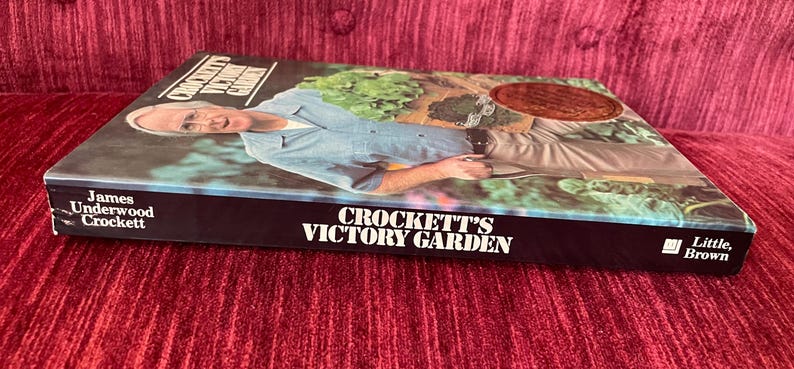 May include: A hardcover book titled Crockett's Victory Garden by James Underwood Crockett. The cover features a photograph of a person in a light blue shirt gardening. The spine and cover display the title in white text against a black background.