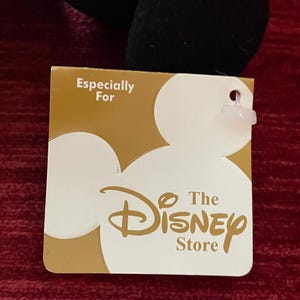 May include: A gold tag with the text "Especially For The Disney Store" and a white Mickey Mouse silhouette.