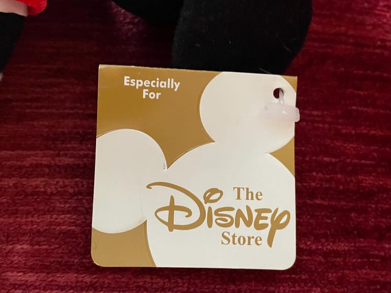May include: A gold tag with the text "Especially For The Disney Store" and a white Mickey Mouse silhouette.