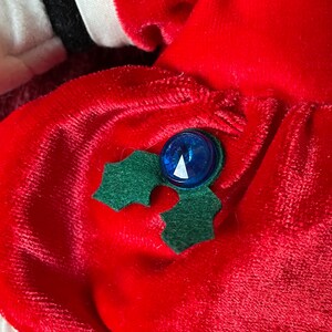 May include: Red velvet dress with a green holly leaf and blue button embellishment.