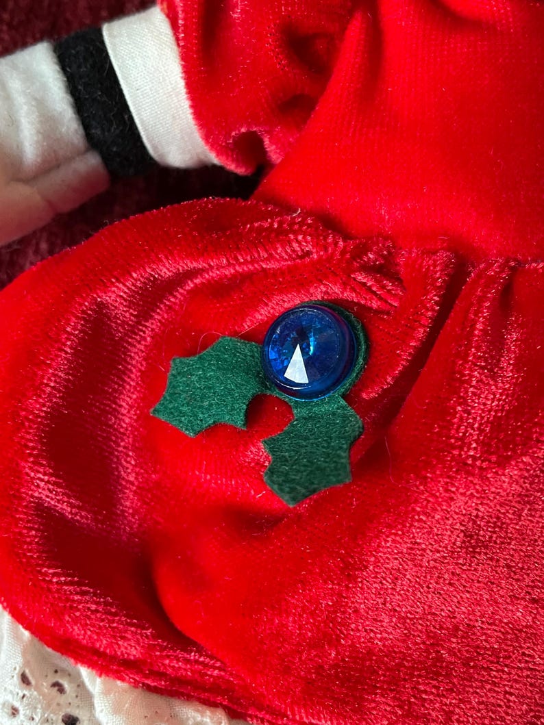 May include: Red velvet dress with a green holly leaf and blue button embellishment.